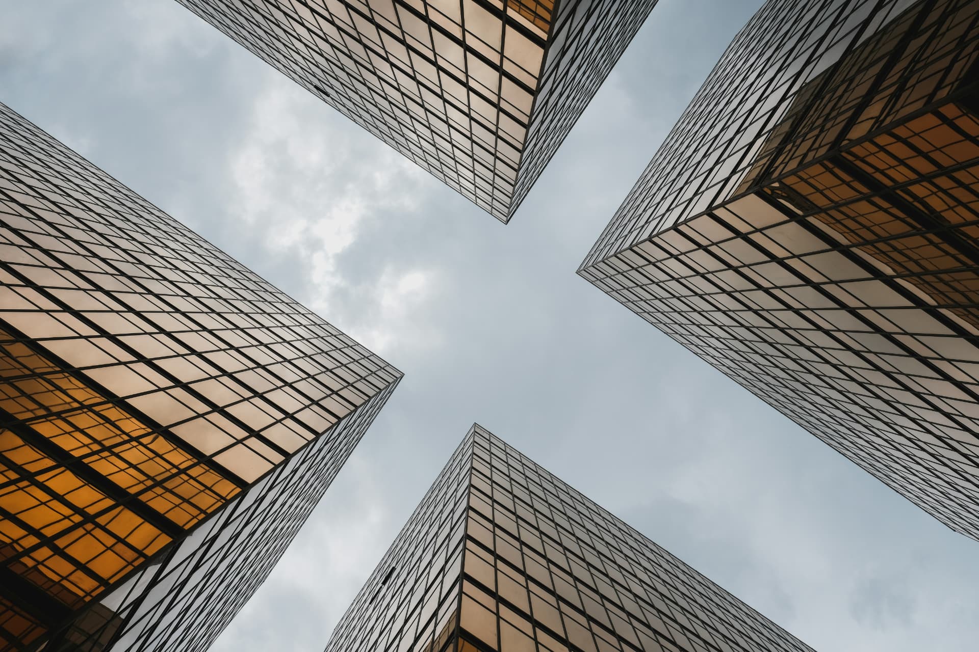 Four glass skyscrapers converging into an X shape against a cloudy sky